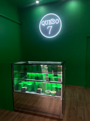 Interior del local Queso 7 con mostrador refrigerado y cartel de neón verde